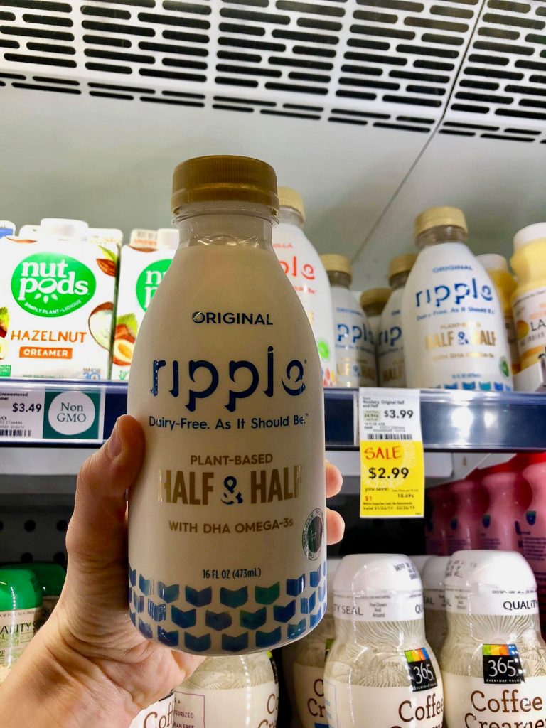 A hand holding a bottle of Ripple unsweetened half & half at Whole Foods. 