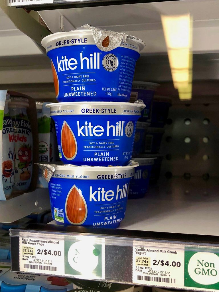 Three containers of Kite Hill vegan greek yogurt stacked on top of each other on a shelf at Whole Foods. 