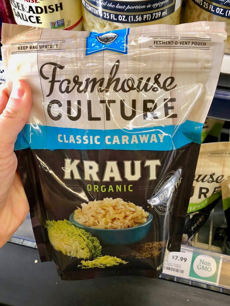 A hand holding a bag of Farmhouse Culture sauerkraut at Whole Foods. 