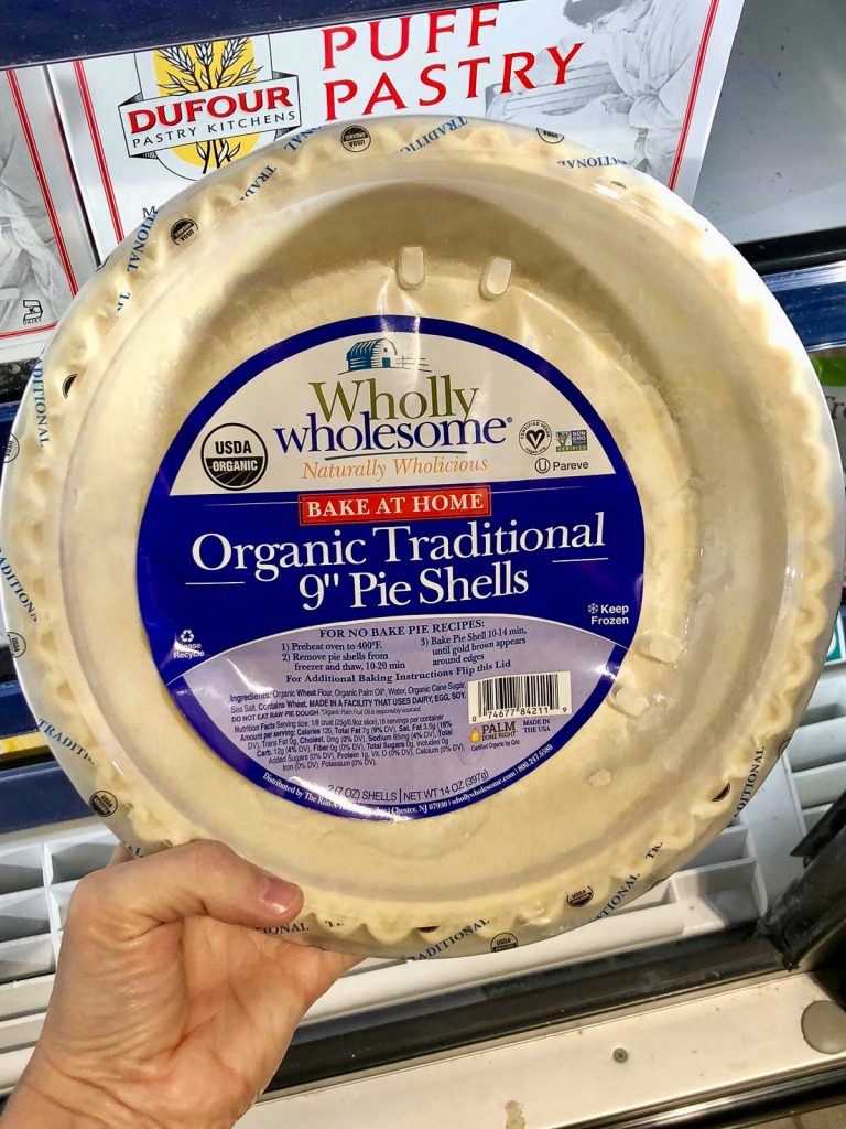 A hand holding a package of Wholly Wholesome vegan pie crusts at Whole Foods. 