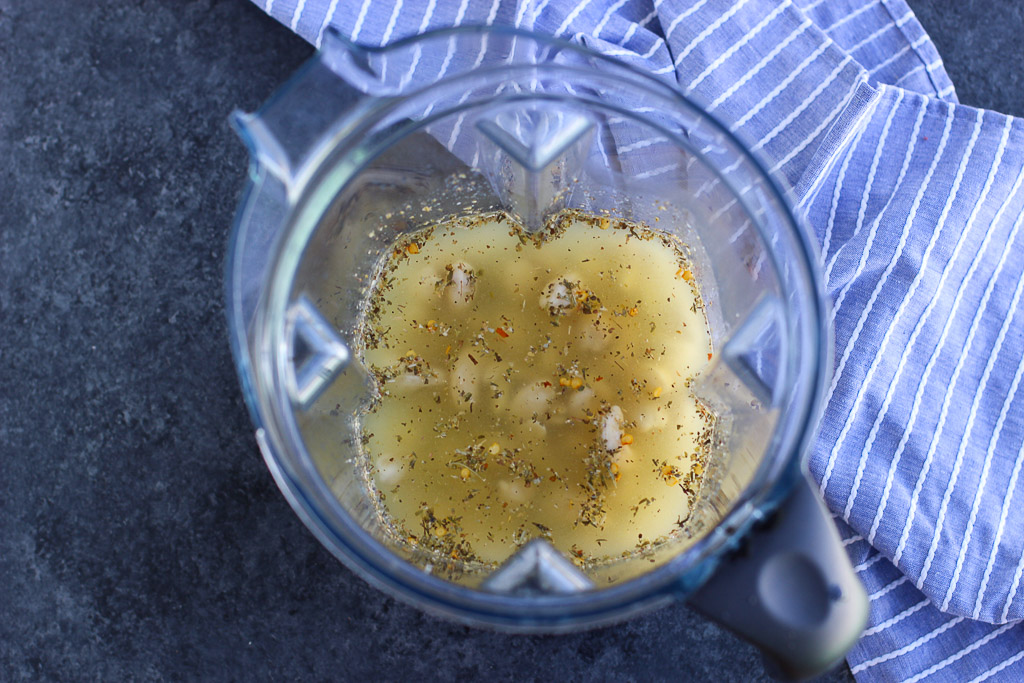 A large blender cup filled with ingredients to make dairy free alfredo sauce next to a blue striped napkin.