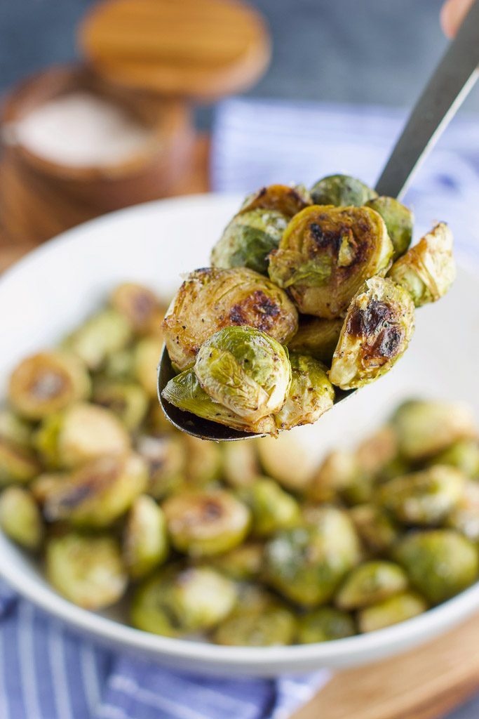 A hand holding a spoonful of brussels sprouts over a filled white bowl. 