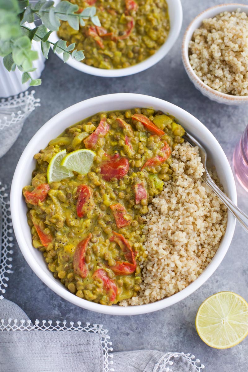 A white bowl filled with quinoa and green curry lentils surrounded by small bowls of food and a gray napkin.