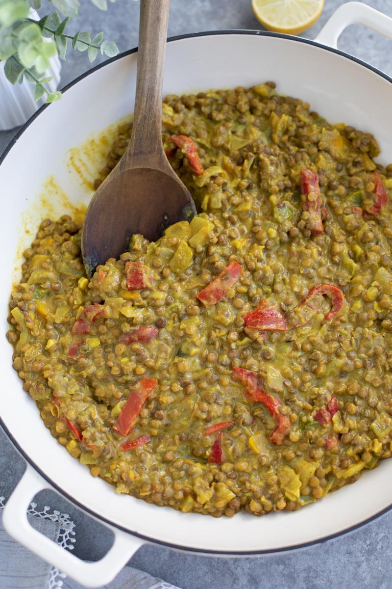 A white pan filled with green lentils and a wooden spoon on a gray background.