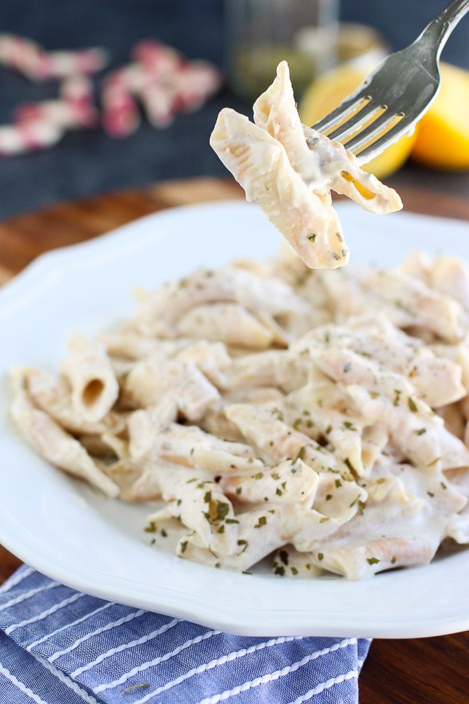 A fork holding a few noodles tossed in creamy cashew alfredo sauce over a white plate next to a blue striped napkin. 
