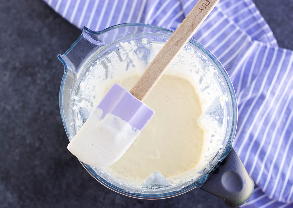 A large blender cup filled with blended cream sauce next to a blue striped towel. 