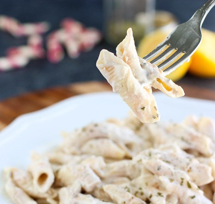 A fork holding a few noodles tossed in creamy sauce over a white plate next to a blue striped napkin. 