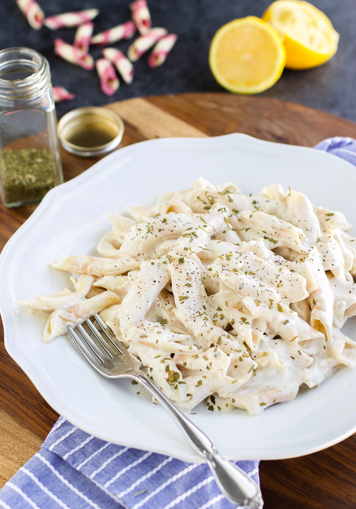 A white plate filled with pasta next to a blue striped napkin and a lemon.