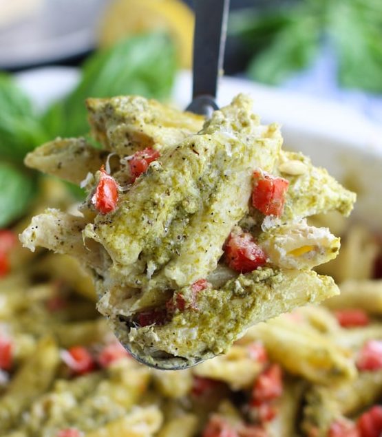 A spoon holding pasta over a white casserole dish that's filled with more pasta.