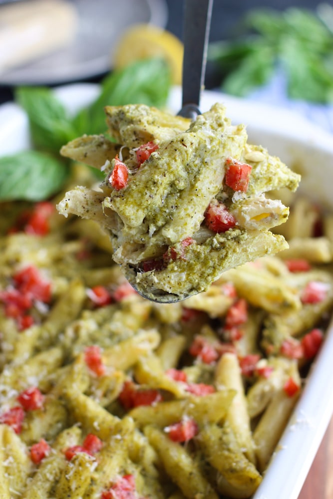 A spoonful of vegan pesto pasta casserole with tomatoes in a white dish. 