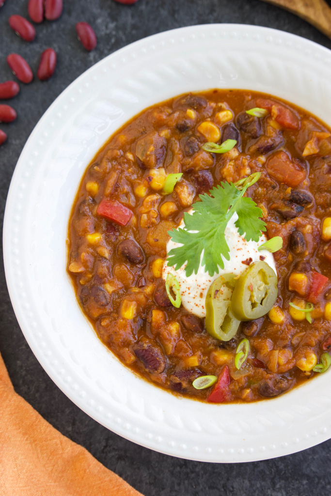 Chili with toppings in a white bowl on a dark background. 