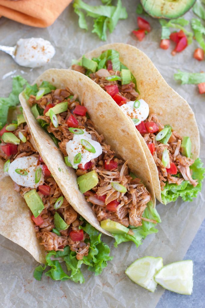 Three tacos topped with vegan sour cream and avocado on parchment paper. 