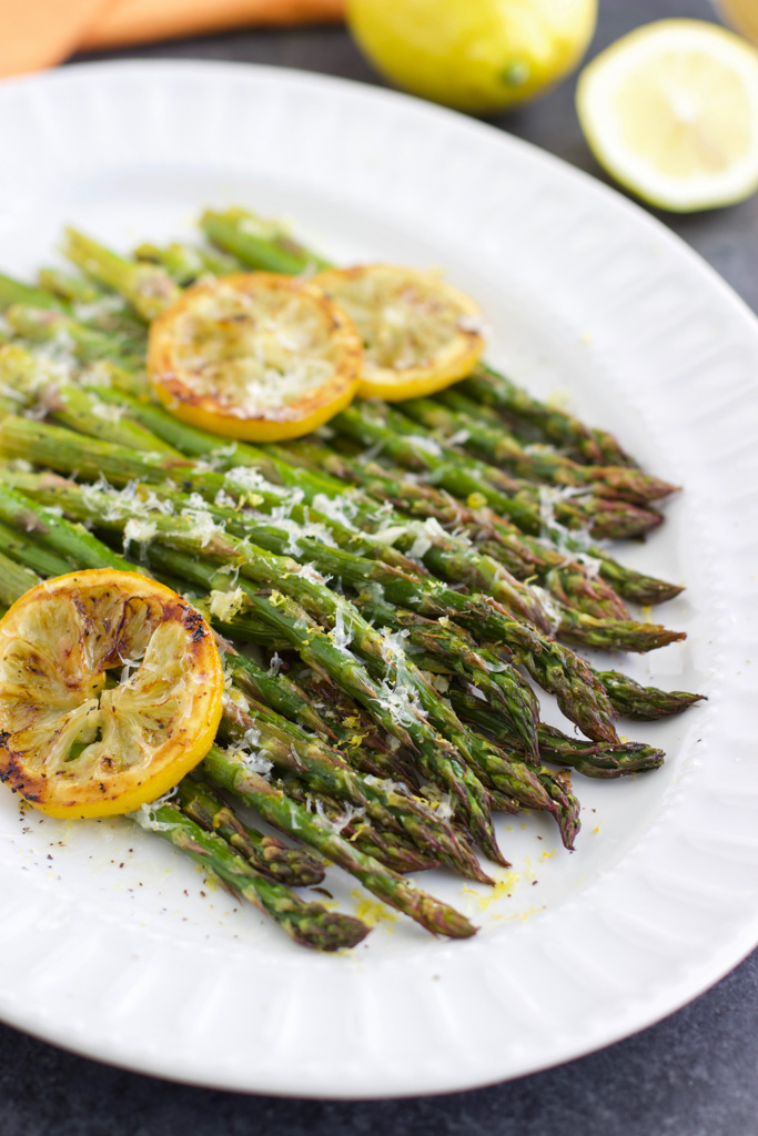 Roasted asparagus with garlic and lemon slices on a large white platter. 