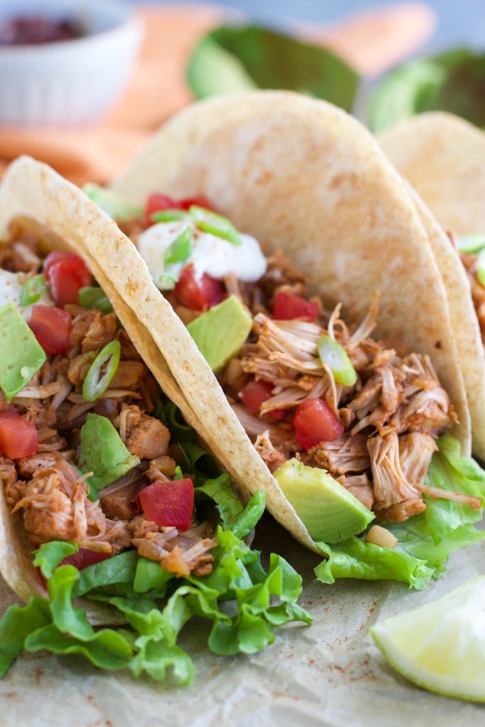 A close up view of a vegan pork taco topped with avocado, green onions, and vegan sour cream.
