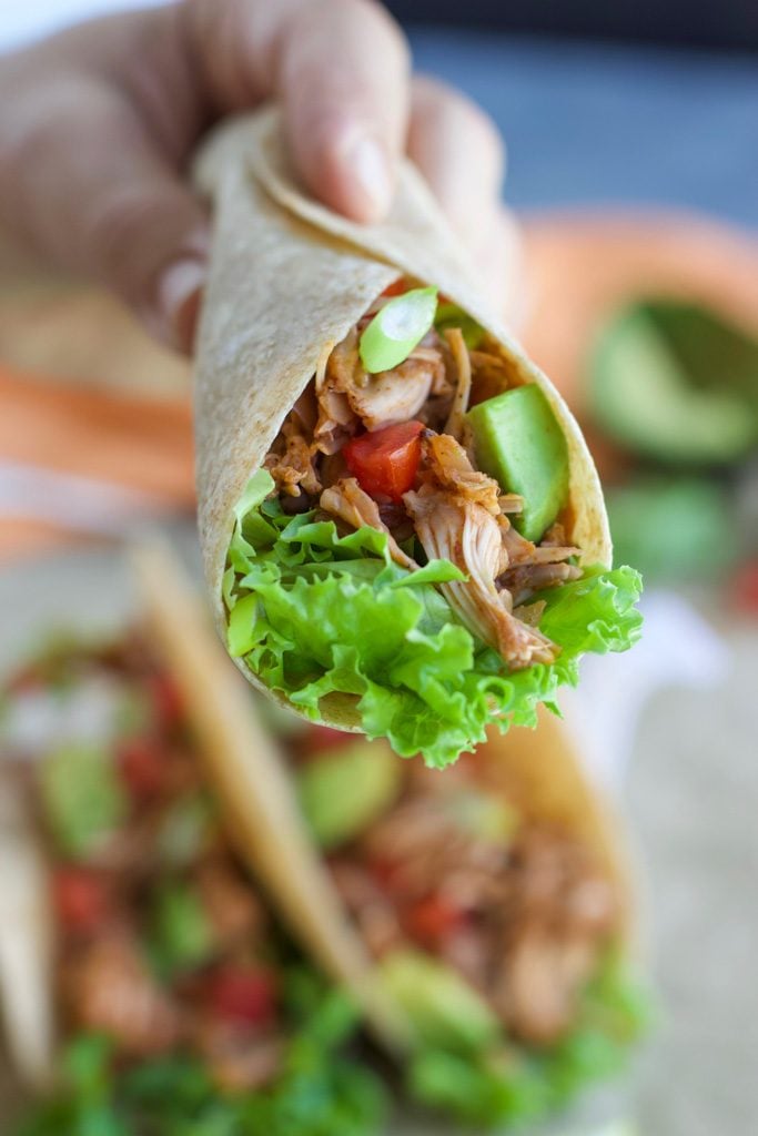 A hand holding a taco over a platter of more tacos.