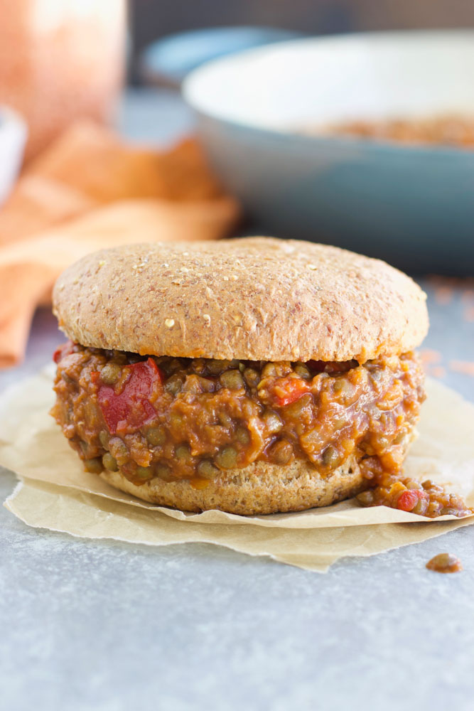 A vegan lentil sloppy Joe sandwich on a piece of parchment paper on a light grey background.