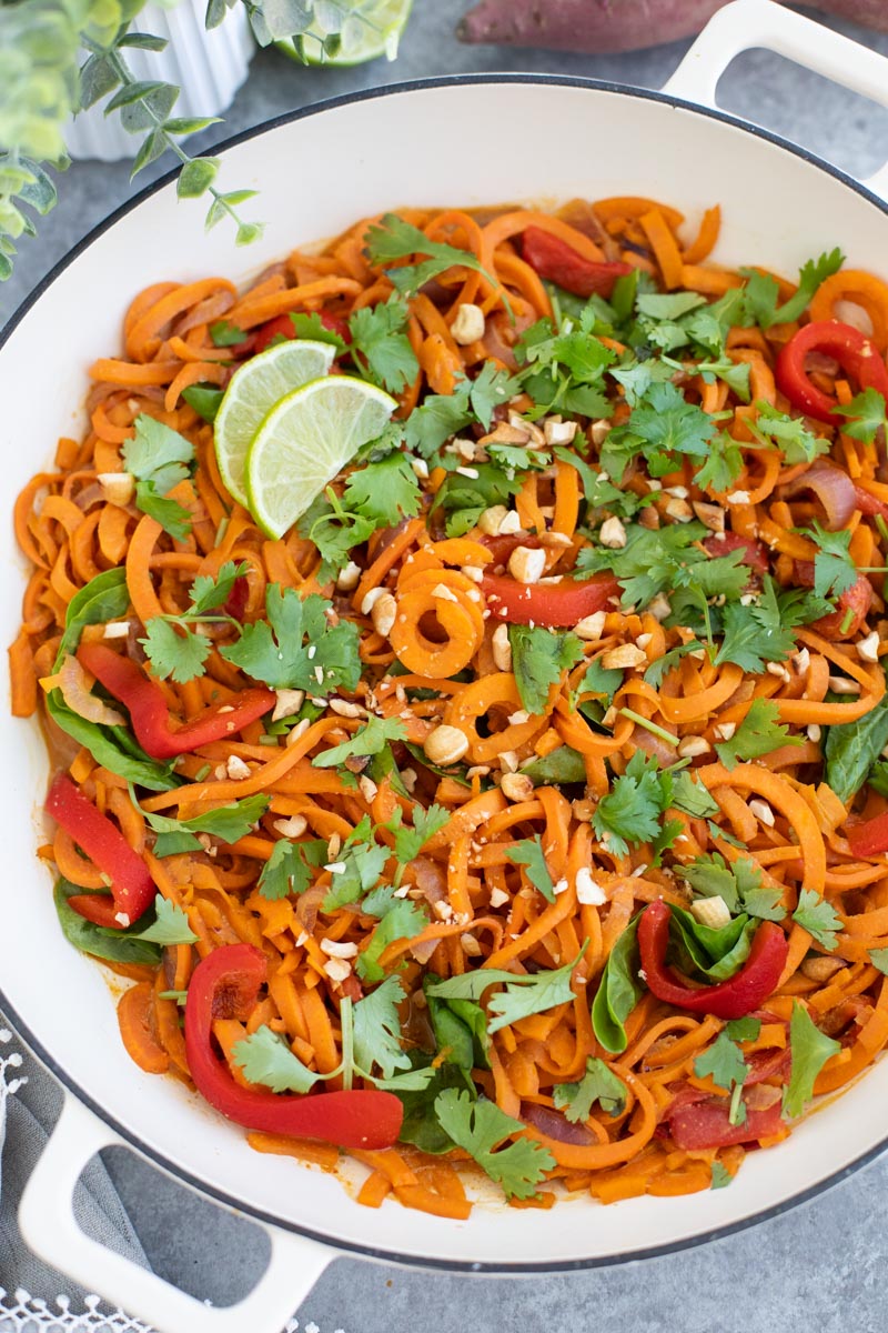 A white pan filled with vegan peanut noodles with lots on toppings on a gray background.