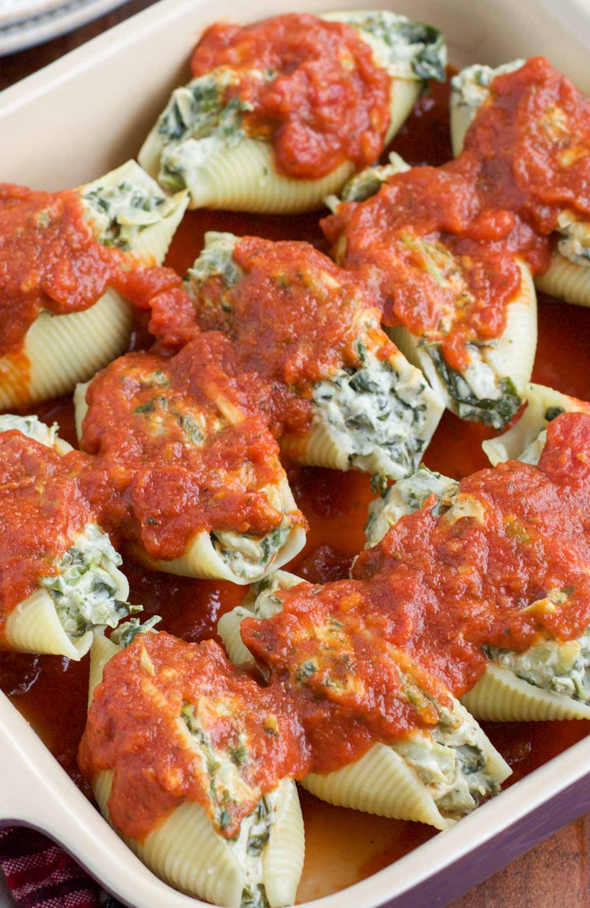 A closeup view of vegan stuffed shells covered in sauce in a casserole dish.
