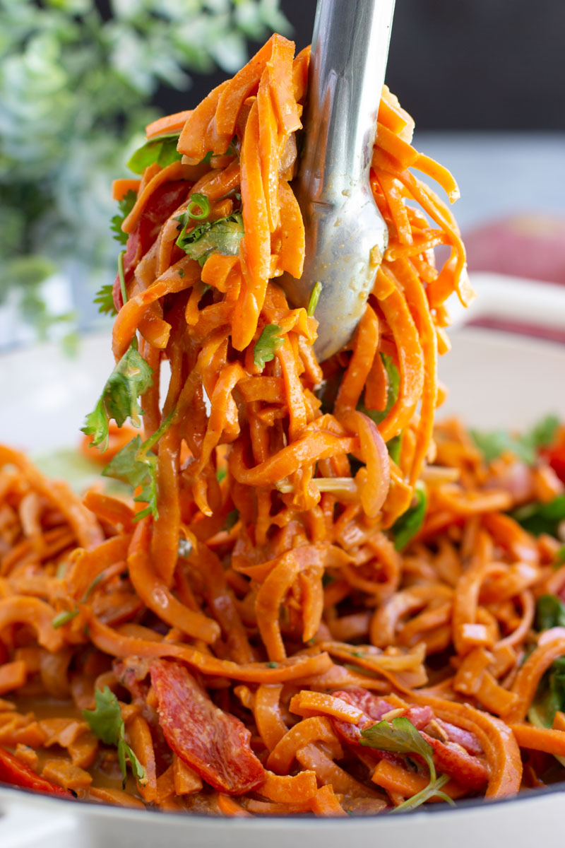 Metal tongs holding a bunch of spoodles over a large white dish. 