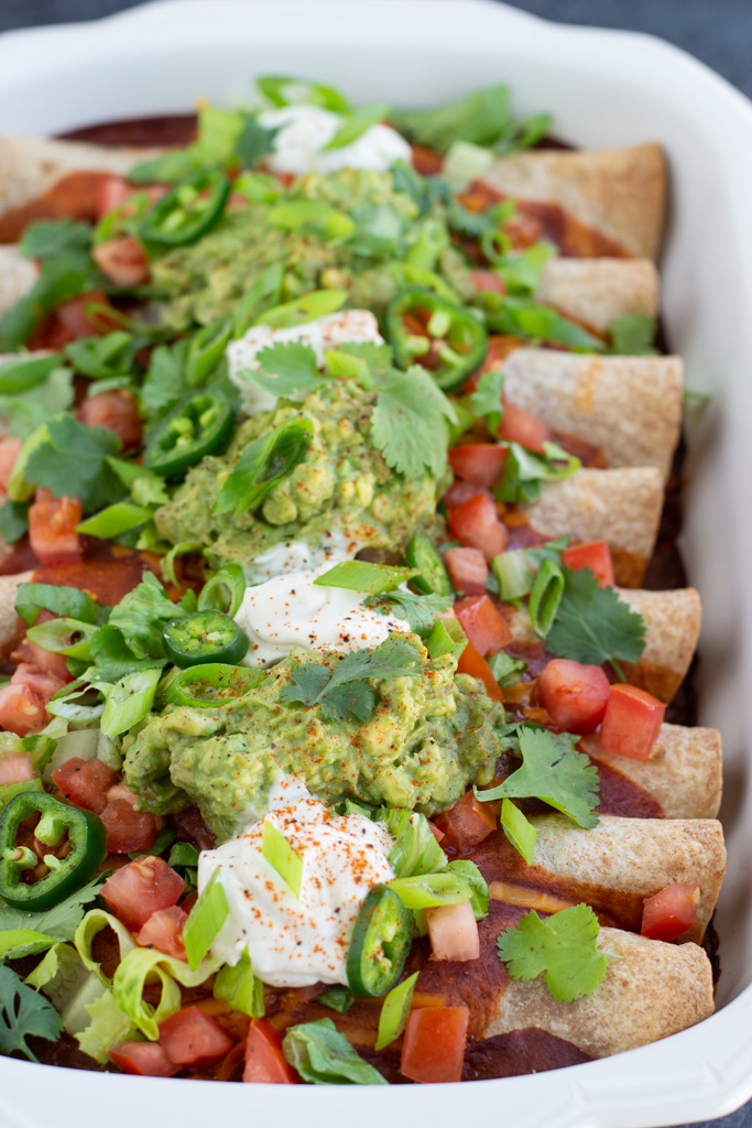 Close up view of enchiladas in a white casserole dish.