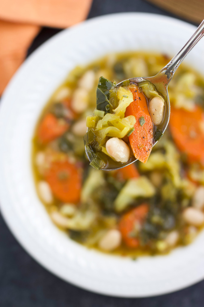 A spoonful of soup over a white bowl next to an orange towel.