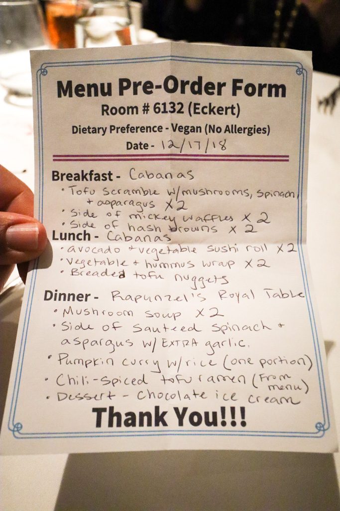 A hand holding a menu pre-order form that has has meal orders written on it during a Disney cruise. 