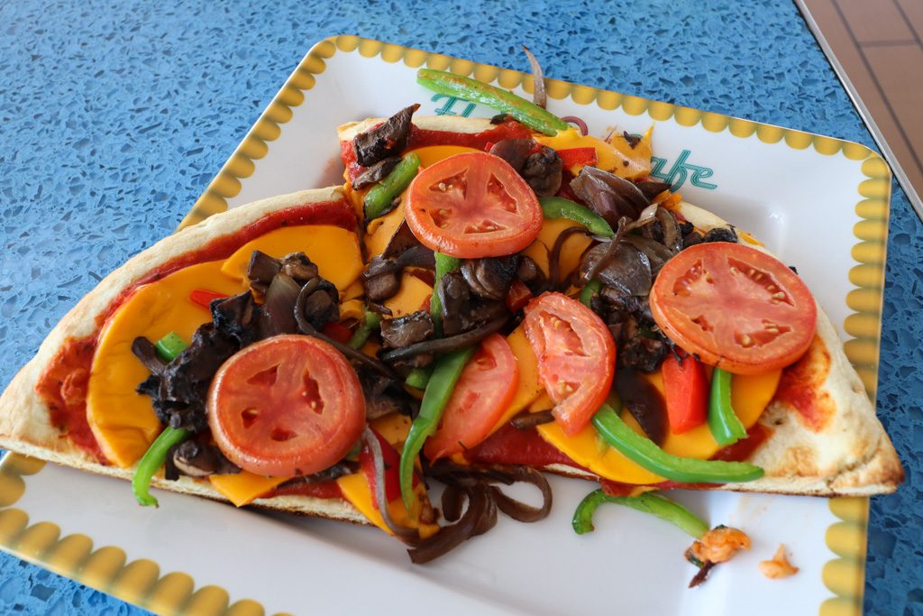 Vegan vegetable pizza on a yellow-trimmed plate sitting on a textured blue table.