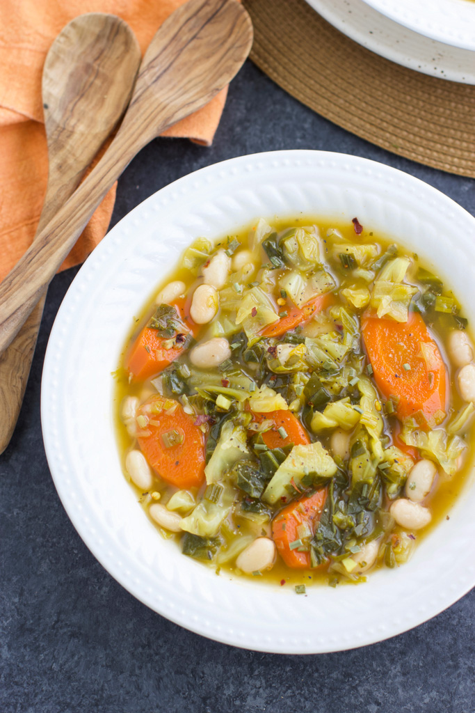 A white bowl filled with soup next to an orange towel and two wooden spoons on a dark textured background.