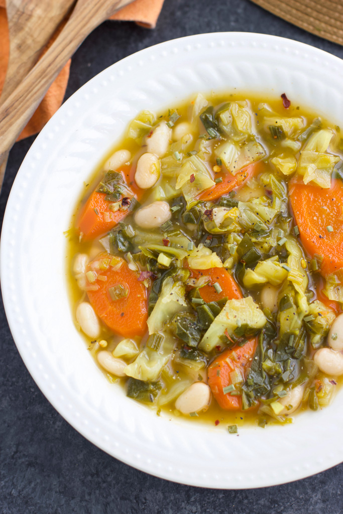 A white bowl filled with vegan cabbage soup on a dark textured background.