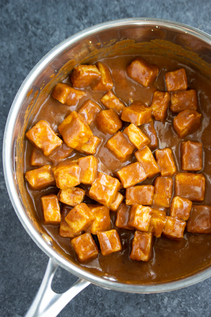 A pot filled with tofu tossed in a lot of brown sauce on a dark background.