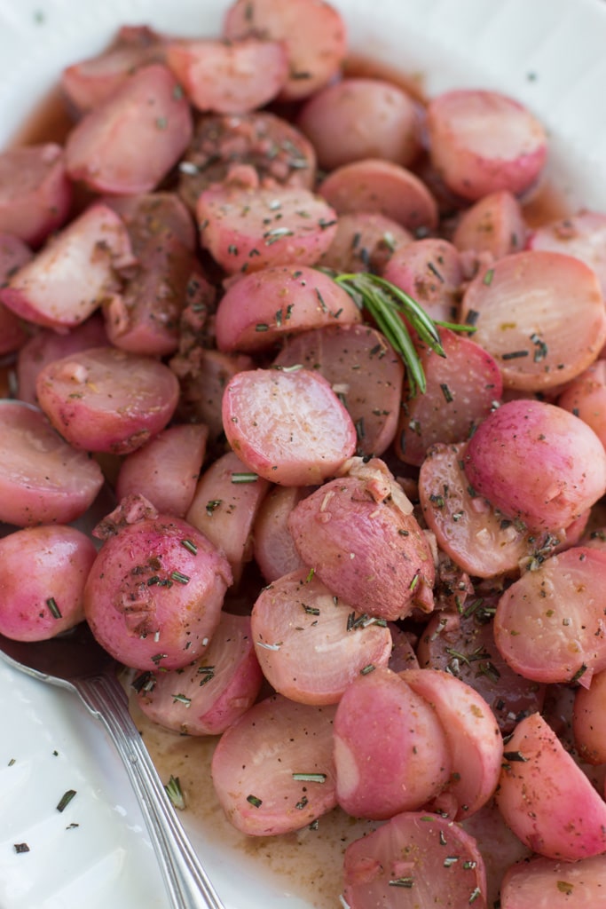 A white serving platter filled with vegan keto roasted radishes that are sprinkled with fresh rosemary. 