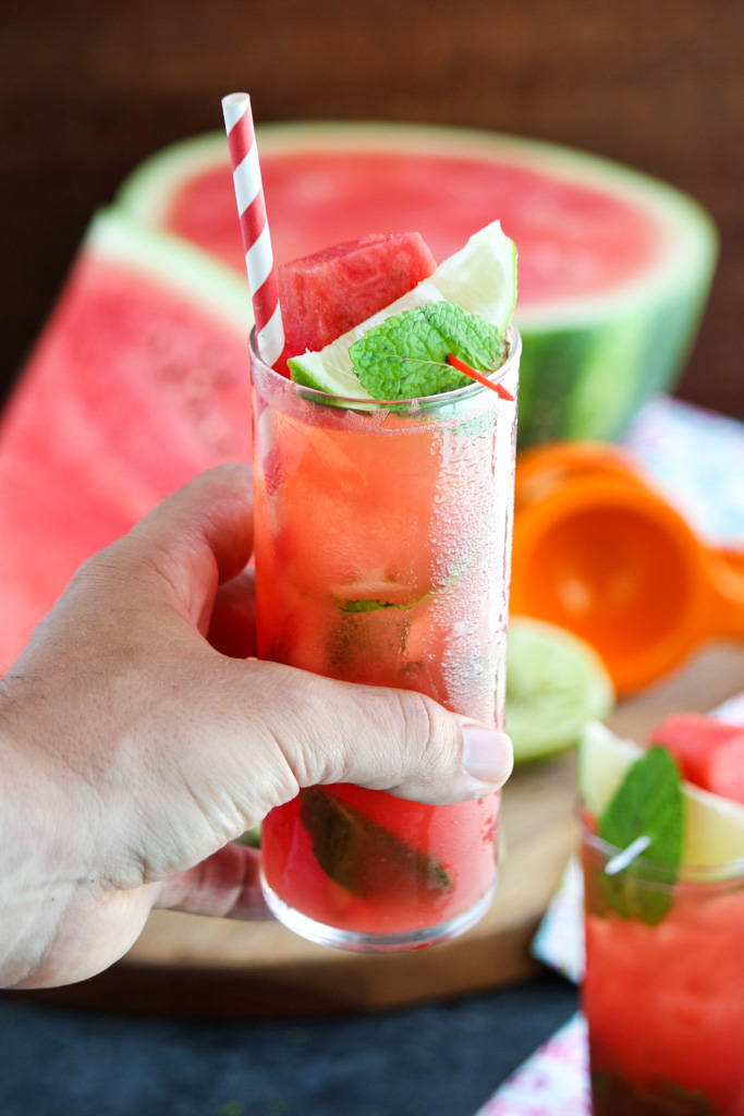 A hand holding a watermelon Moscow mule in a tall glass with a red striped straw.