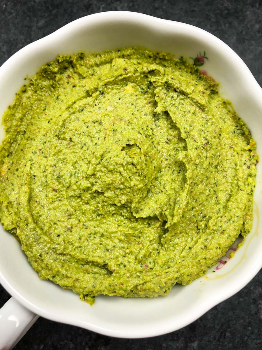 A white cup filled with green vegan pesto on a dark background.