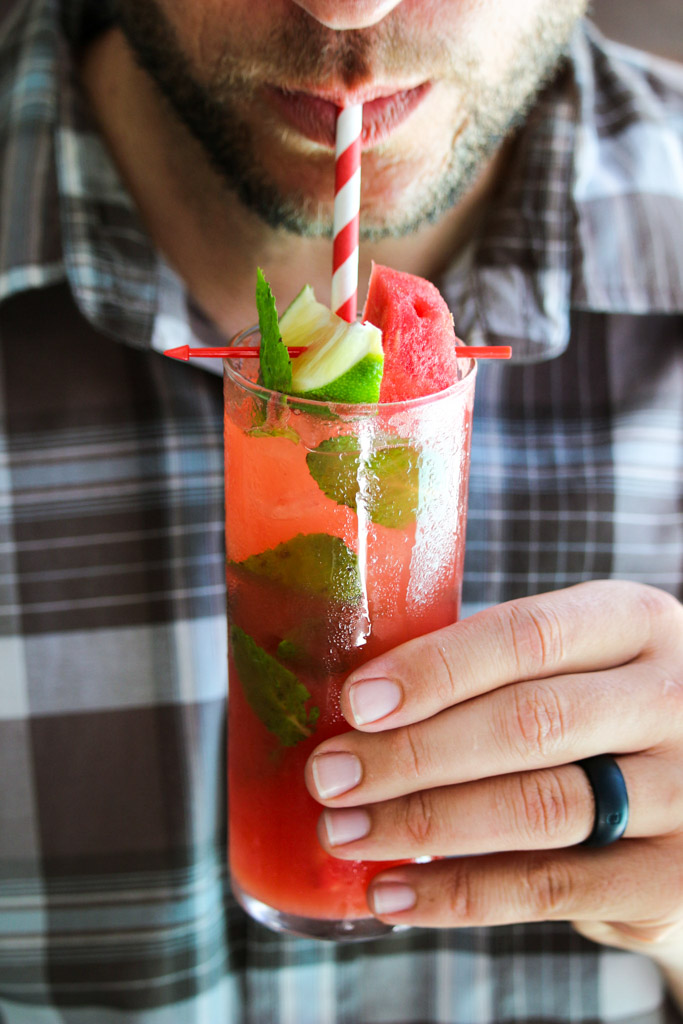 A man drinking a watermelon Moscow mule through a paper straw out of a glass. 