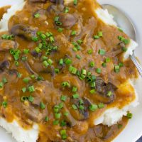 A white bowl filled with mashed potatoes, mushroom gravy, and chives.