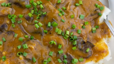 A white bowl filled with mashed potatoes, mushroom gravy, and chives.