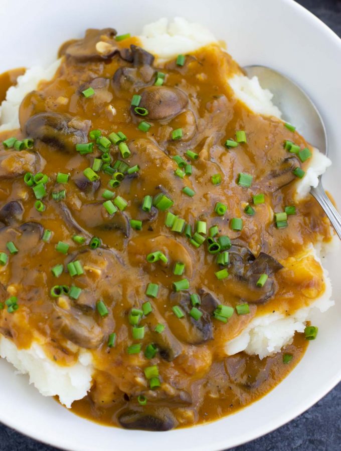 A white bowl filled with mashed potatoes, mushroom gravy, and chives.