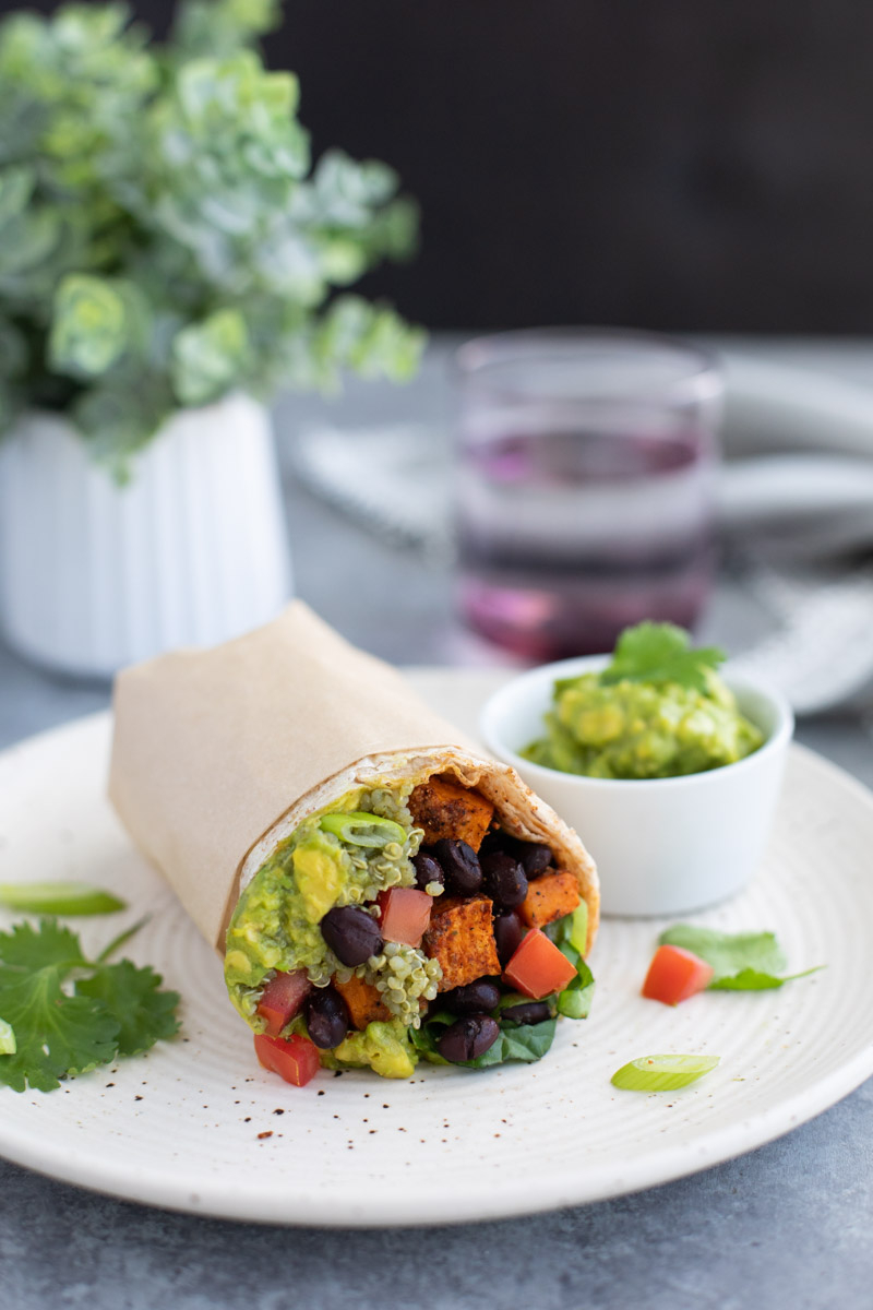 A inside shot of a vegan burrito on a white plate on a gray background.