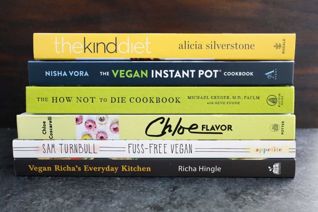 A stack of six vegan cookbooks on a dark background.