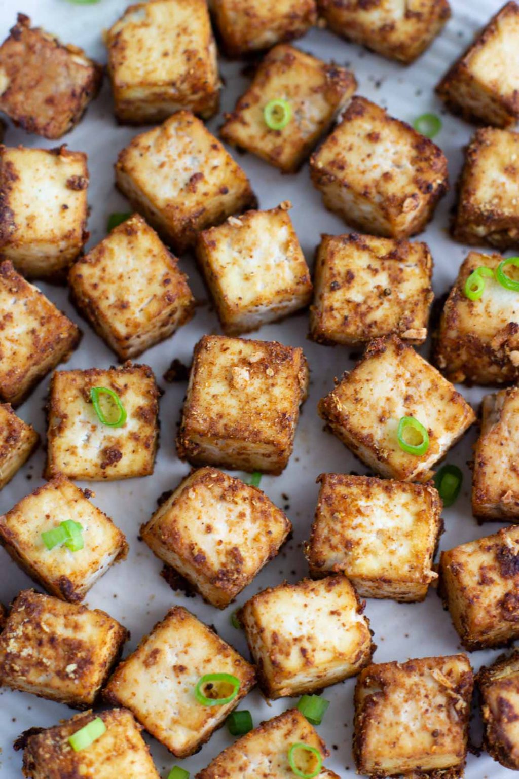 A close-up view of a tray filled with crispy baked tofu topped with sliced green onions. 