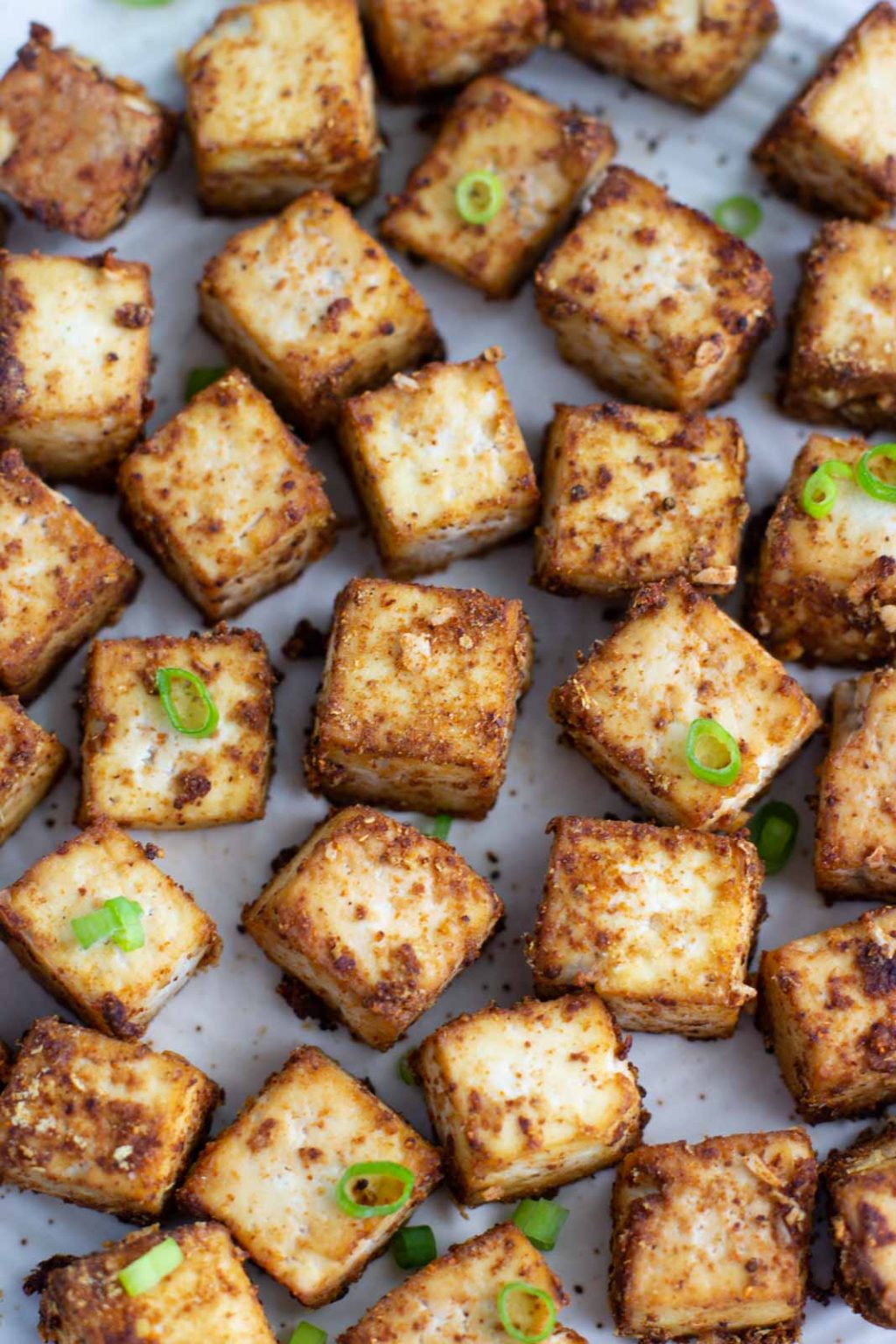 A close-up view of a tray filled with crispy baked pieces of tofu topped with sliced green onions.