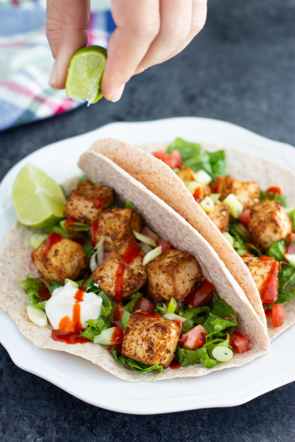 Two tofu wraps on a white plate with a hand squeezing a lime over the top. 