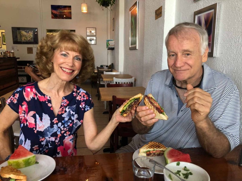 A man and woman touching their sandwiches together over a wooden table.