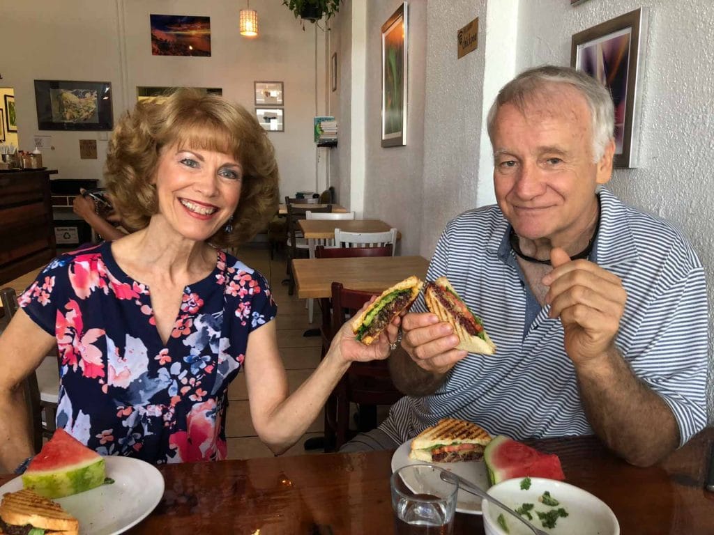 A man and woman touching their sandwiches together over a wooden table. 