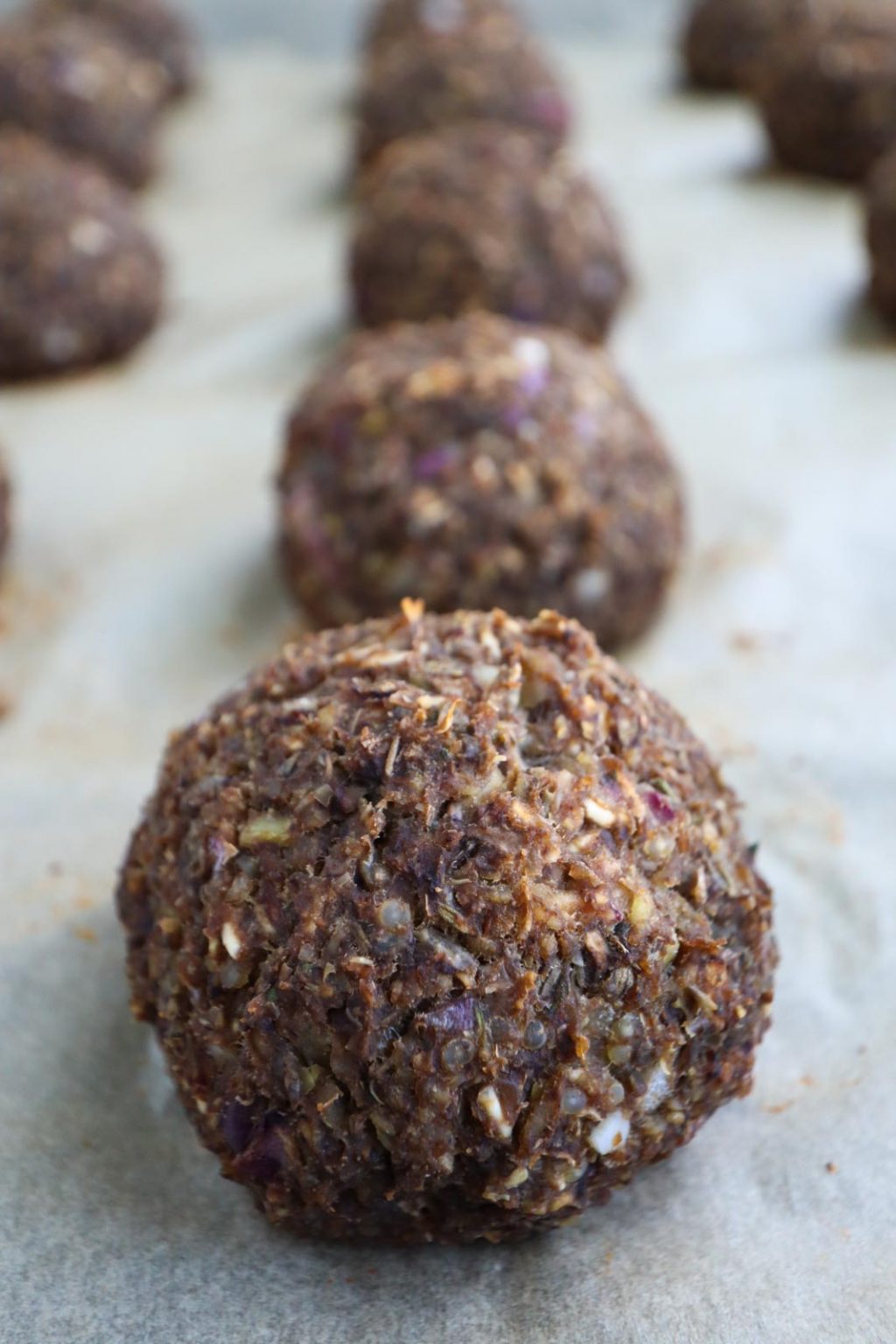 A close up of a lentil meatball next to rows of other meatballs on parchment paper. 