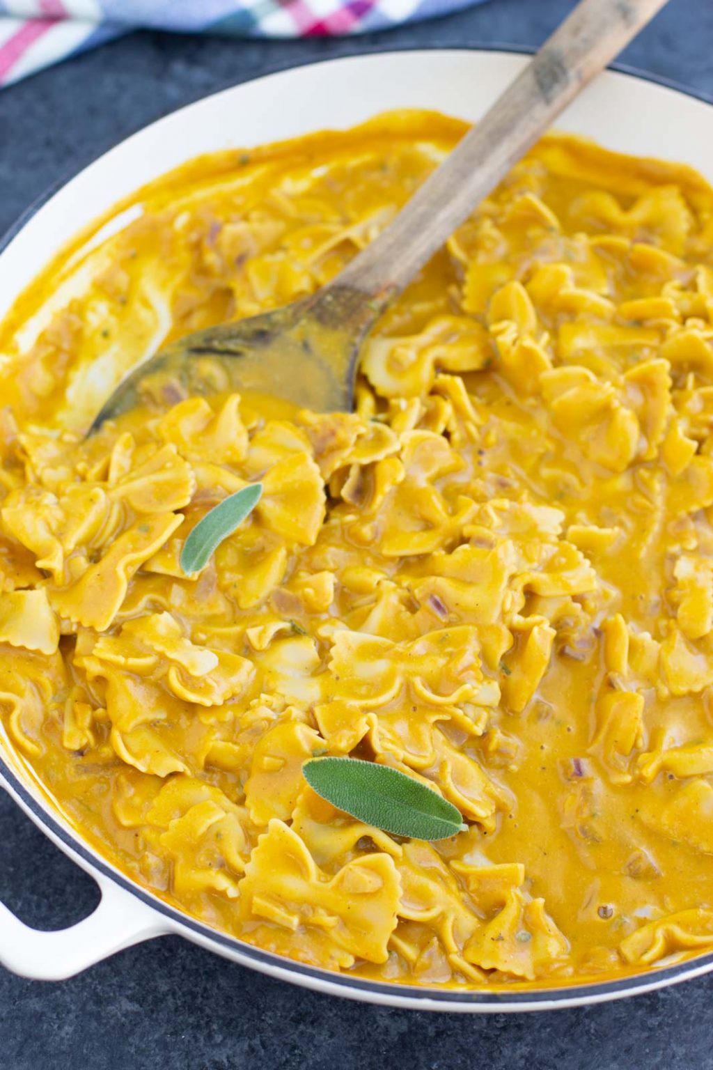 A white pan filled with pasta that's being stirred by a wooden spoon.