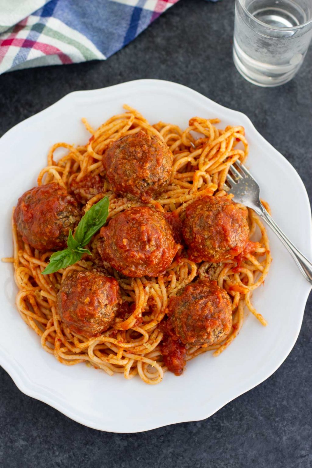 A white plate filled with vegan meatballs and spaghetti on a dark background. 