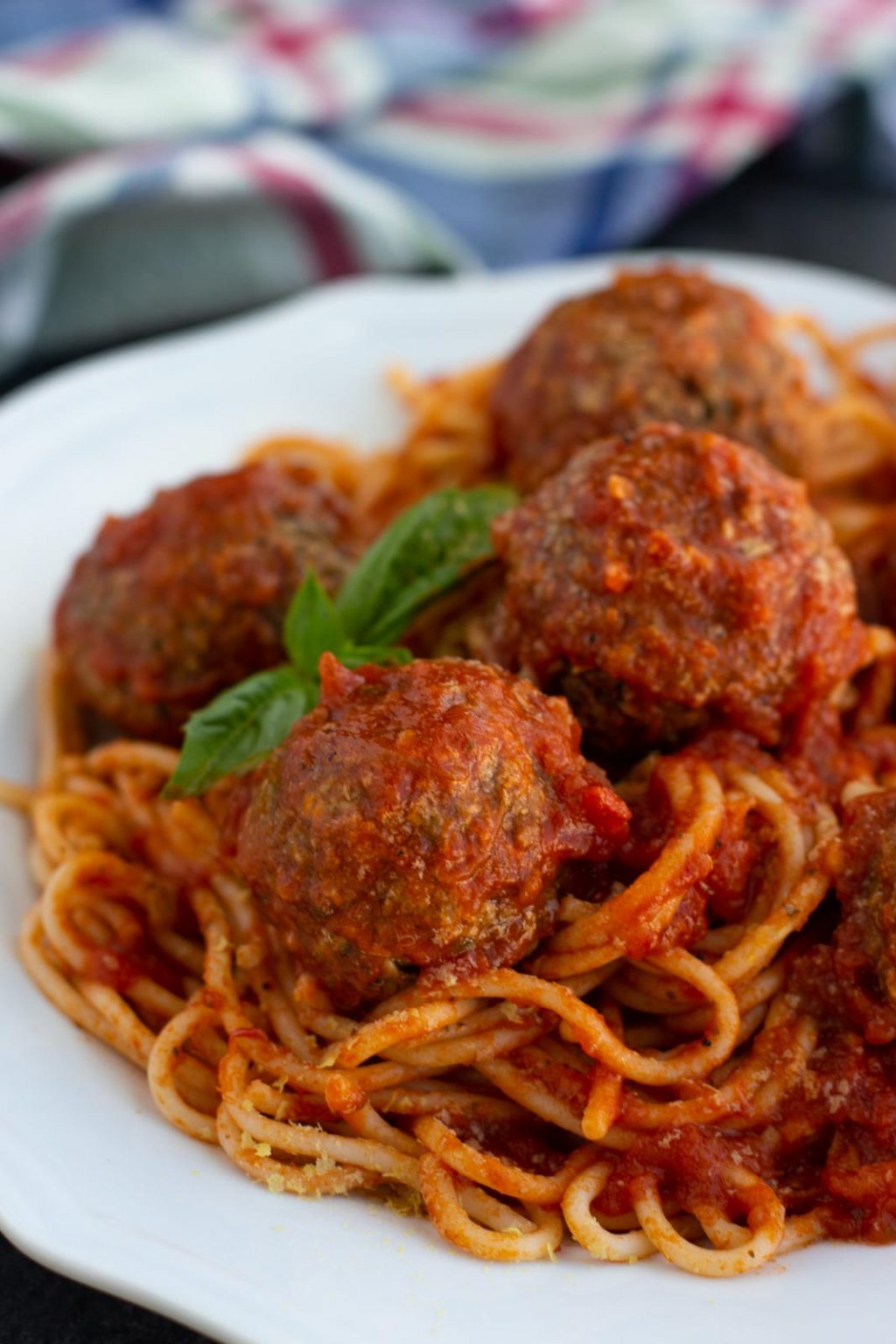 A white plate filled with spaghetti and lentil meatballs with fresh basil.