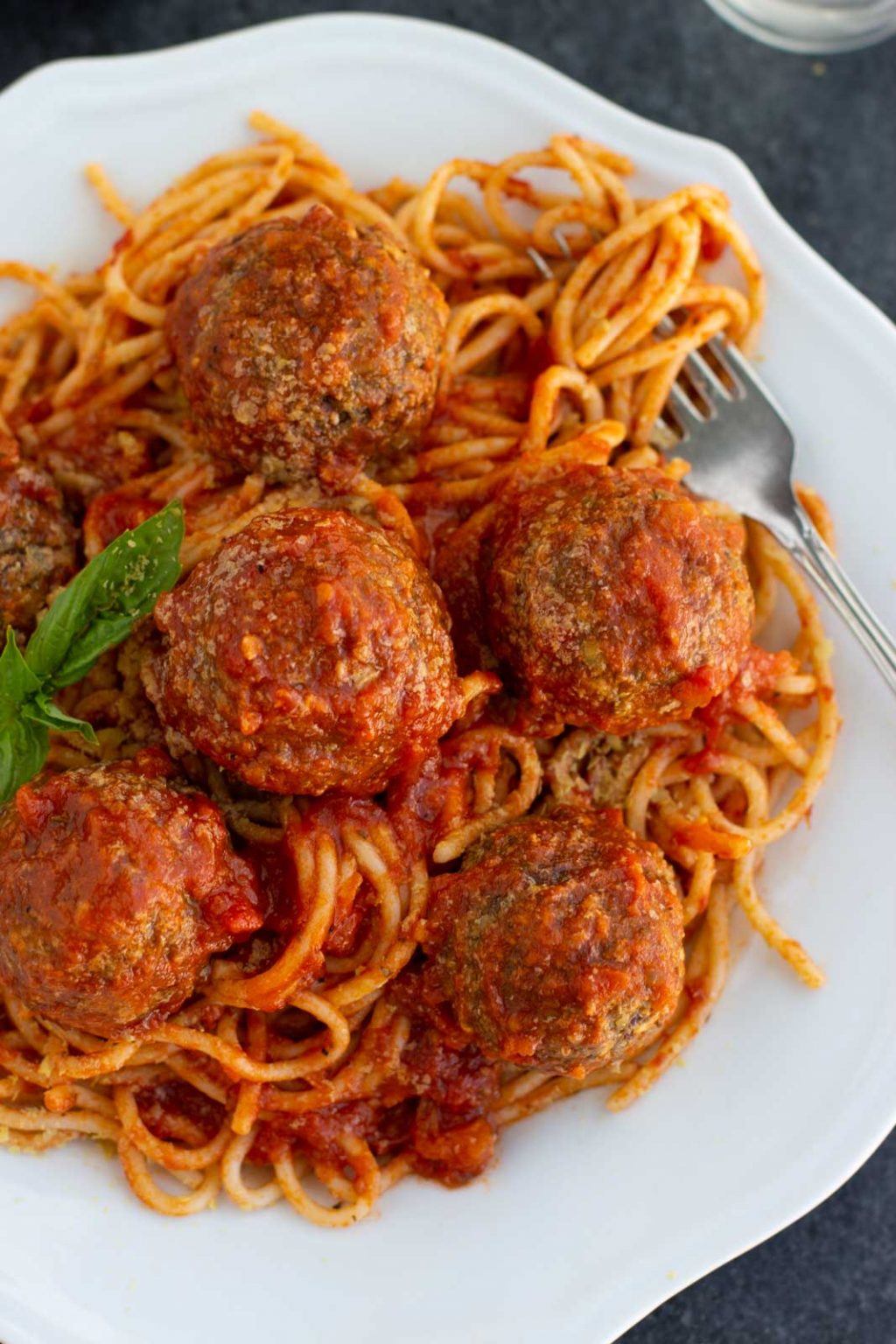 A white plate filled with vegan meatballs and spaghetti on a dark background.