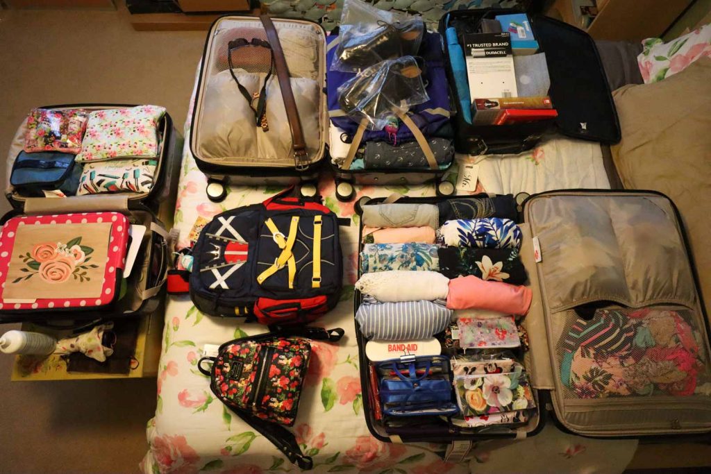 Multiple suitcases opened on a bed so you can see all of the clothes and items that are packed inside. 